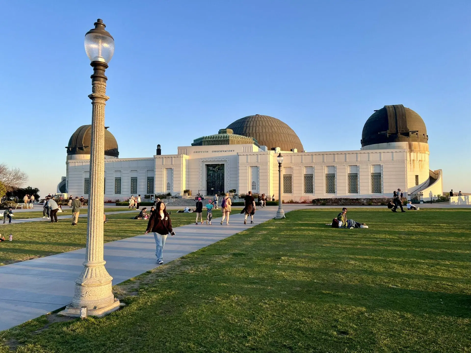 Observatorio Griffith en luz dorada al final del día, con visitantes en el césped frente a la explanada