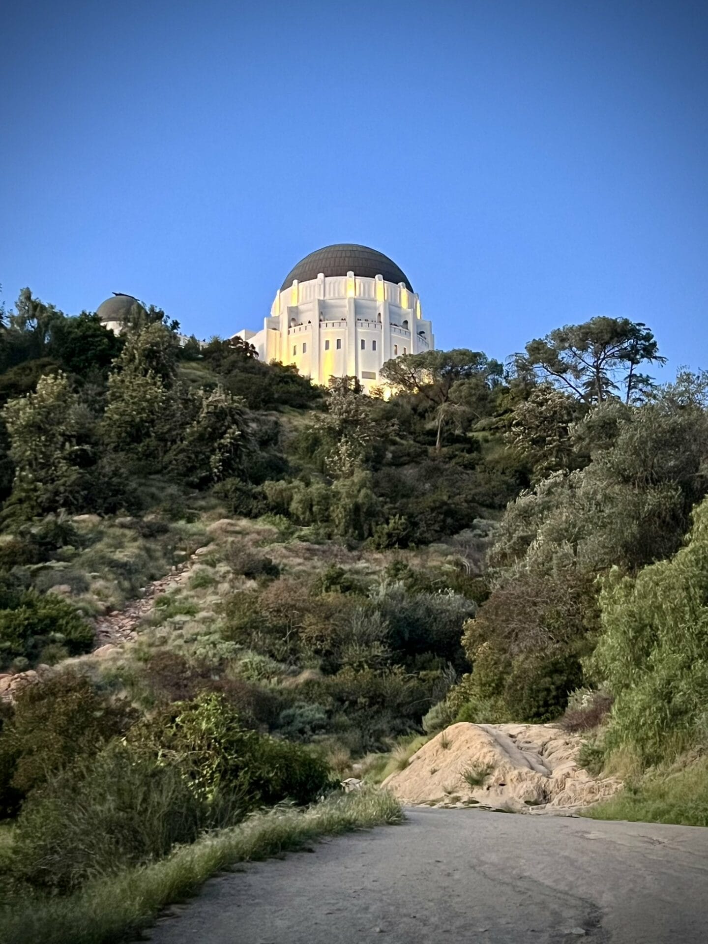 Vista lateral del Griffith Observatory iluminado, fotografiado desde una curva más abajo en la carretera de Griffith Park