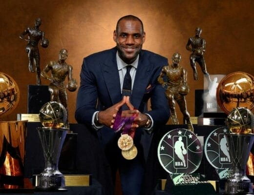 LeBron James posant en costume devant ses trophées : titres de champion NBA, trophées MVP et médailles d’or olympique