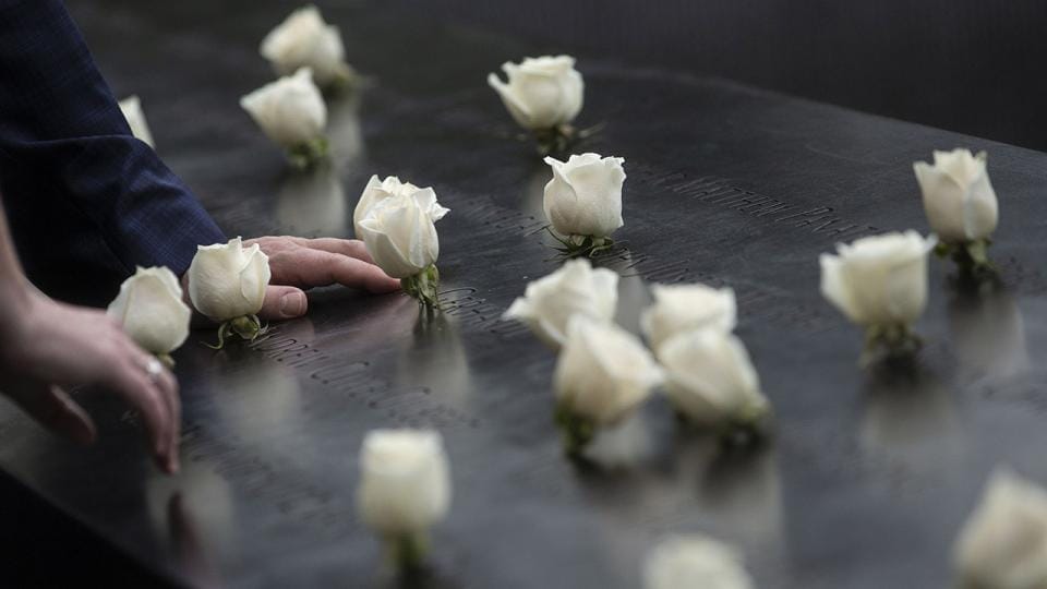Main posée sur un nom gravé au Mémorial du 11 Septembre entouré de roses blanches en hommage aux victimes