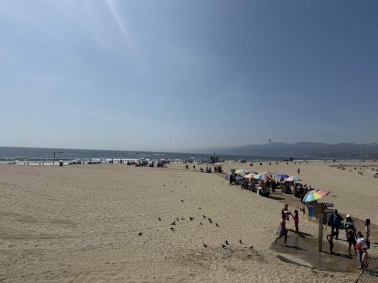 Plage de Santa Monica avec vendeurs ambulants sous parasols colorés et vue sur les montagnes