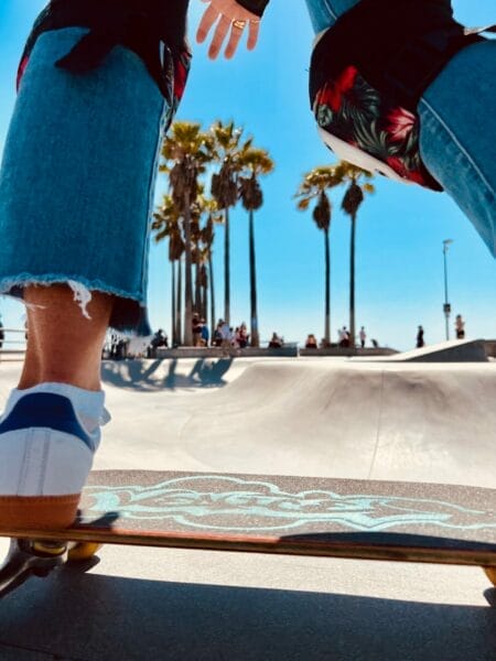 Skateboarder en action au skatepark de Venice Beach avec palmiers en arrière-plan, sous le soleil californien