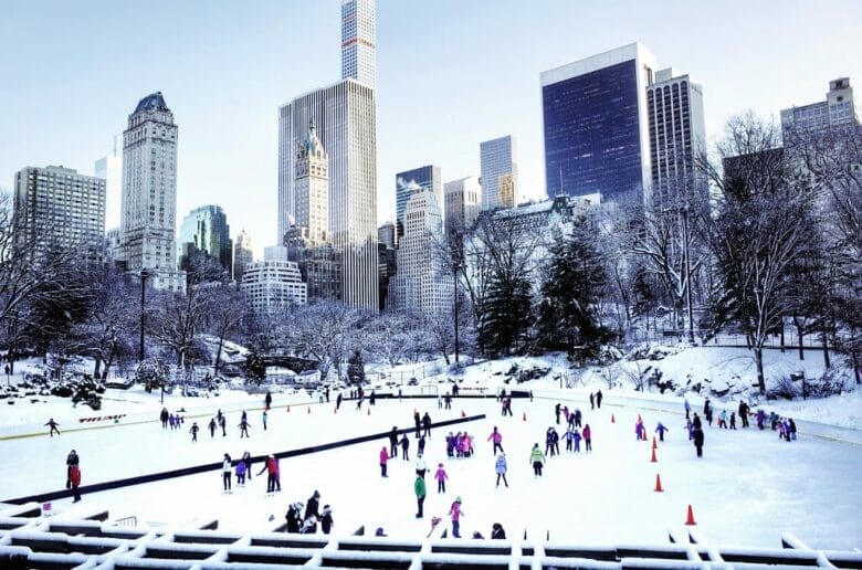 Patineurs sur la Wollman Rink de Central Park enneigé, skyline de Midtown New York en arrière-plan