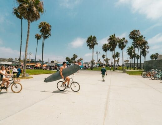 man holding surfboard white riding bicycle