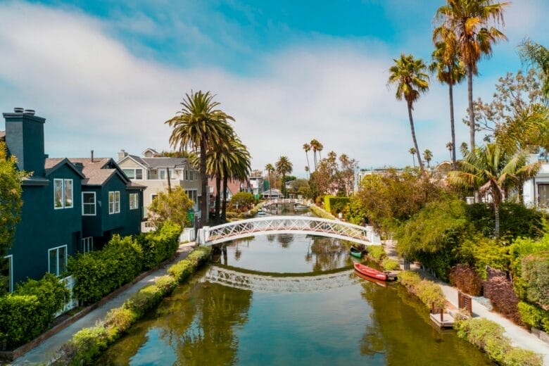 Vista de los Canales de Venice en Los Ángeles con puente blanco, casas residenciales y palmeras bajo un cielo azul