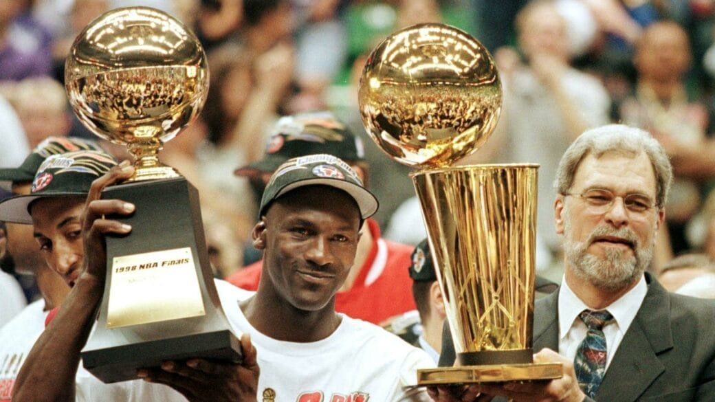 Michael Jordan et Phil Jackson célébrant le sixième titre NBA des Chicago Bulls en 1998, trophées Larry O’Brien et MVP des Finales en main