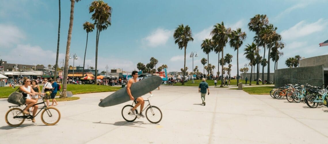 man holding surfboard white riding bicycle